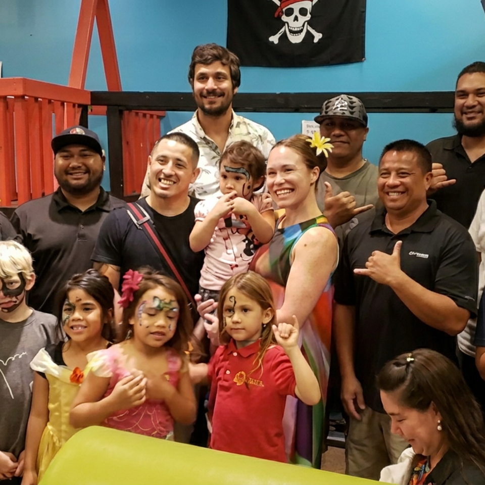 Group of adults and children posing in a colorful indoor play area, with face paint, costumes, and a pirate flag.