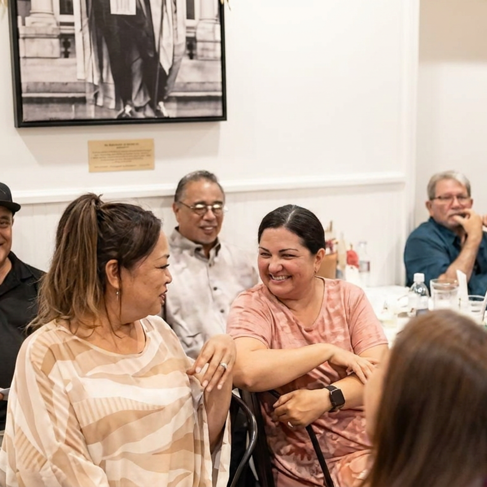 A group of diners smiles and chats around a set restaurant table in a bright dining room.